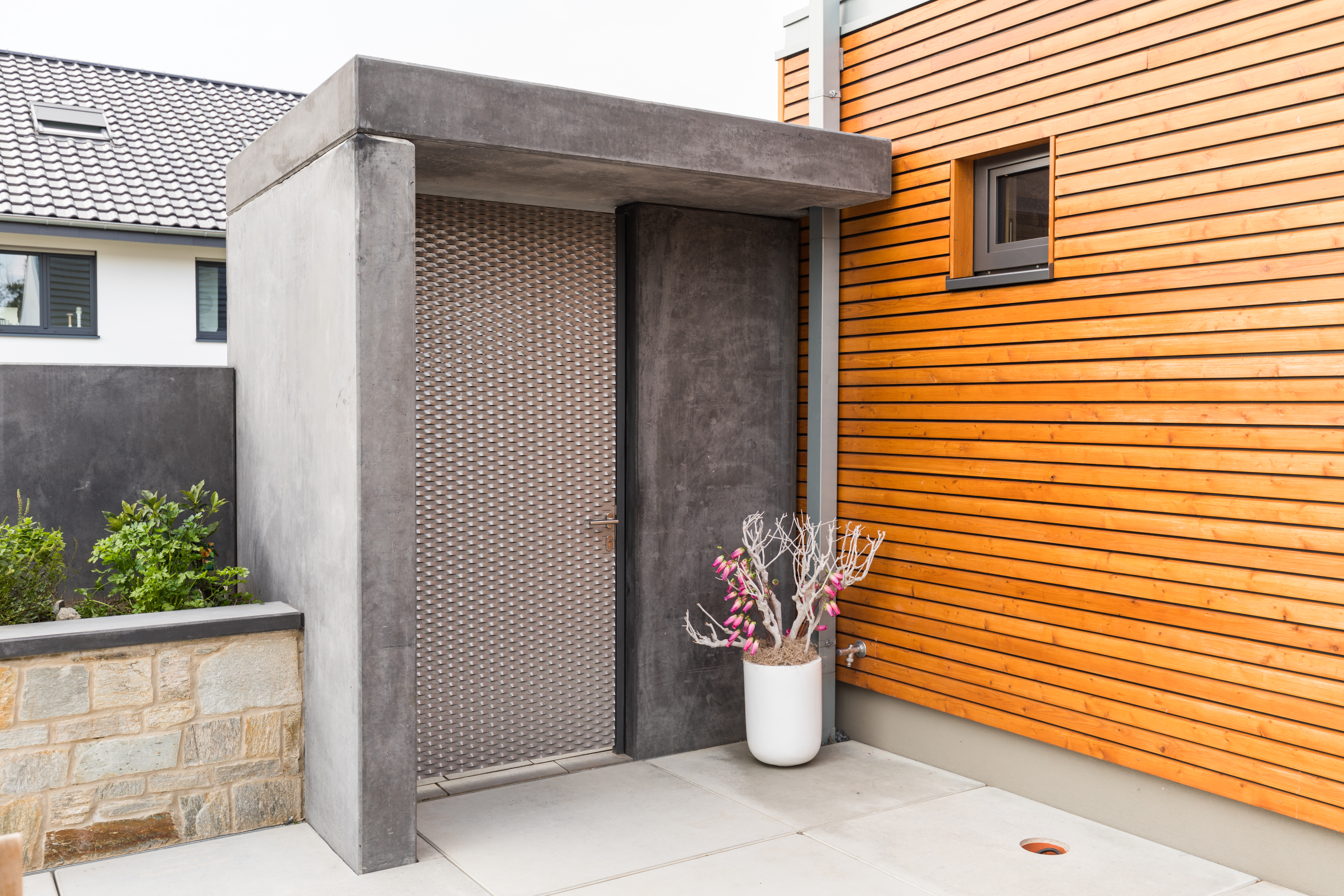 Eingangsbereich aus Beton mit Metalltür und Holzverschalung