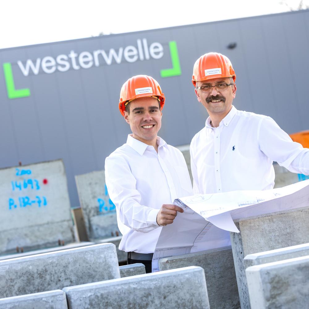 Dwóch pracowników z kaskami i planem przed budynkiem Westerwelle