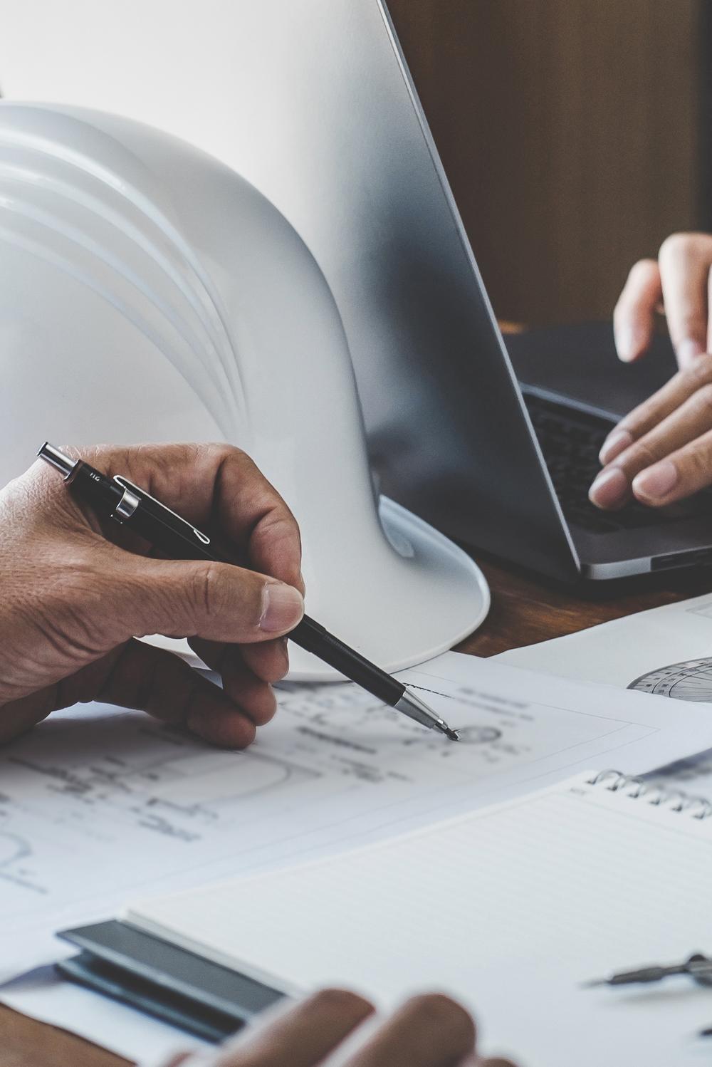 Hände von Architekten, Helm Laptop und Plänen auf einem Schreibtisch